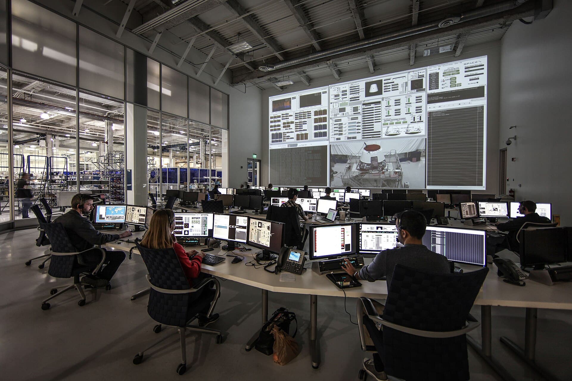 A modern mission control room: rows of consoles with live telemetry, each seat a named controller responsible for a go/no-go call